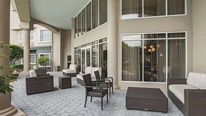 A covered outdoor seating area with wicker furniture and large windows. - La Quinta Inn & Suites by Wyndham Fort Worth North (Fort Worth)