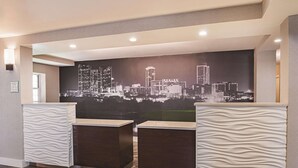 A reception area with a cityscape mural, two reception desks, and a sign indicating a 24-hour check-in service. - La Quinta Inn & Suites by Wyndham Fort Worth North (Fort Worth)