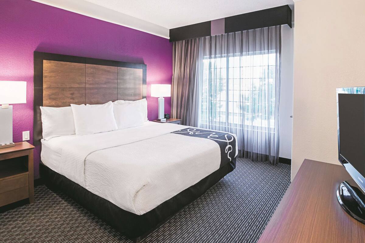 A hotel room with a large bed, a TV, a desk, and a window with curtains.