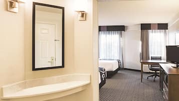 Habitación de hotel con un espejo grande, un lavamanos pequeño, dos camas, un escritorio y un televisor.