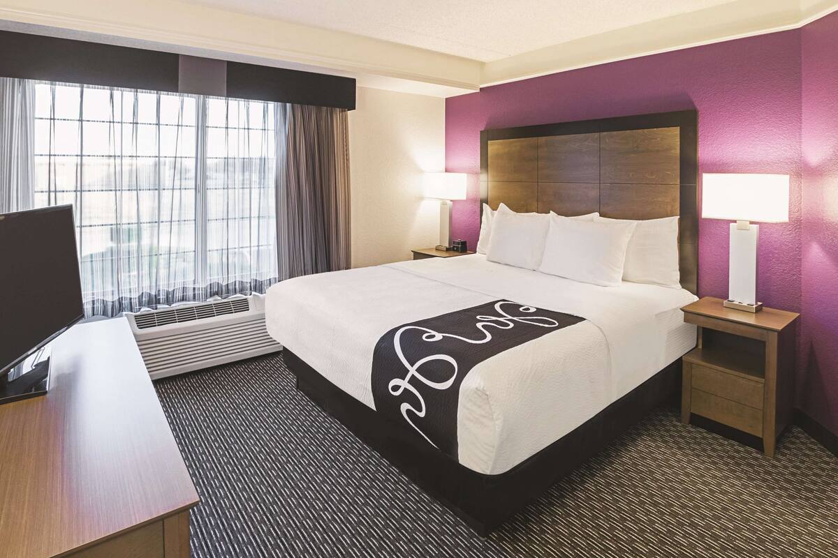 A hotel room with a large bed, a desk, a TV, and a window with curtains.