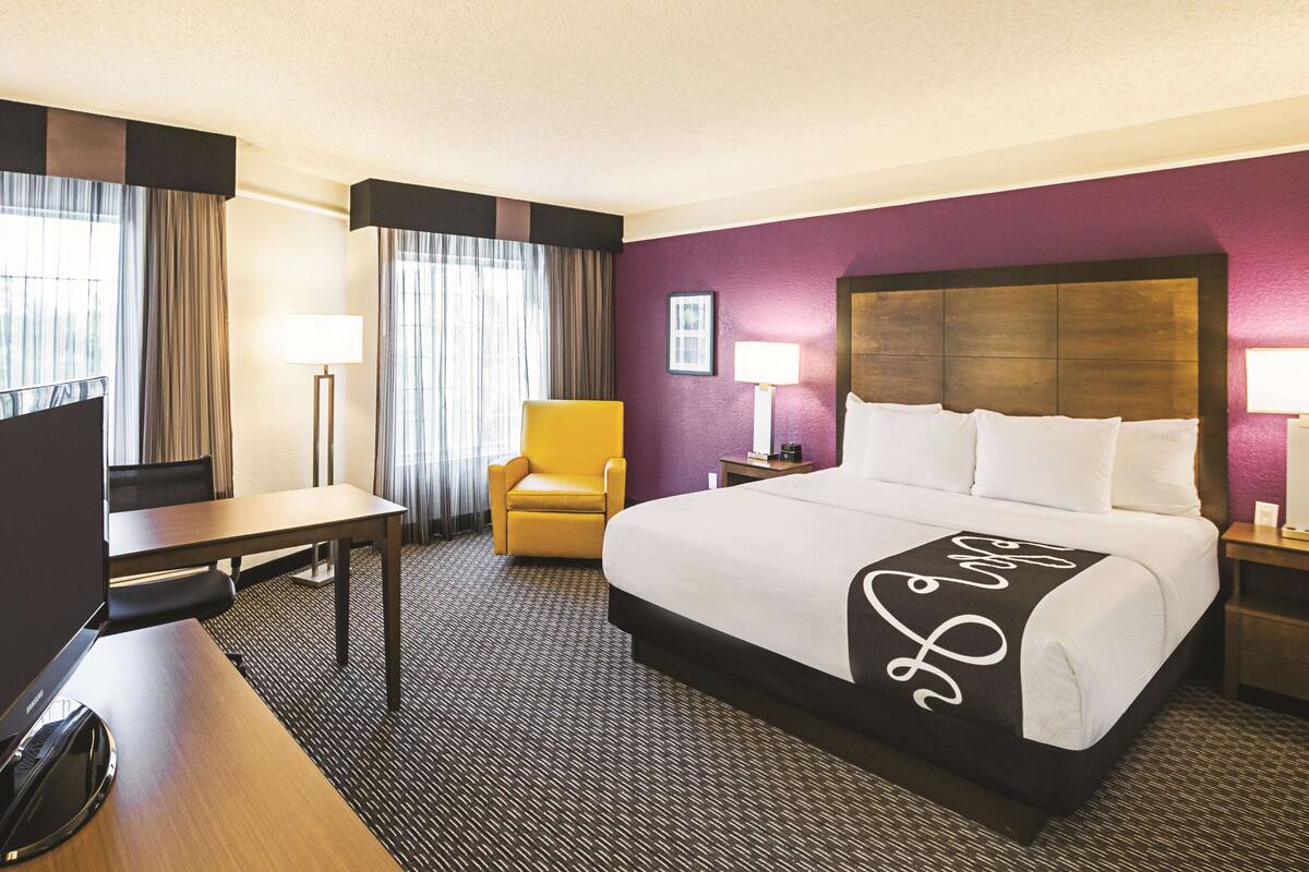 A hotel room with a large bed, a desk, a chair, and a TV.