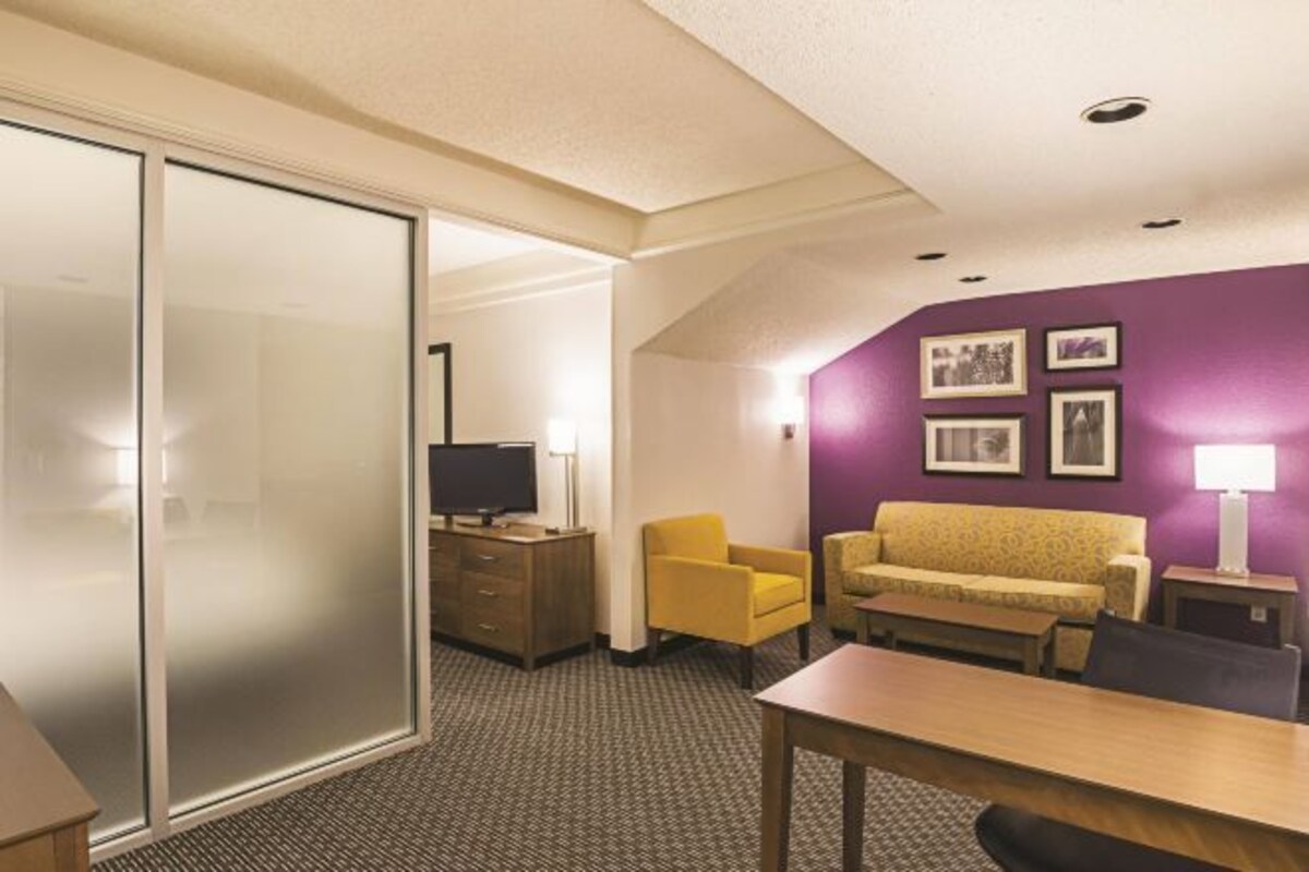 A hotel room with a sliding door, a sofa, a table, a TV, and a lamp.