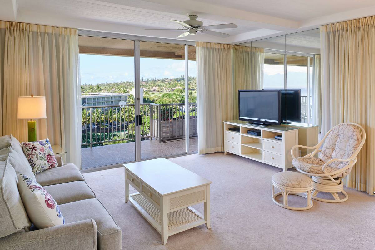 A spacious living room with a sofa, ottoman, coffee table, and a television on a stand.