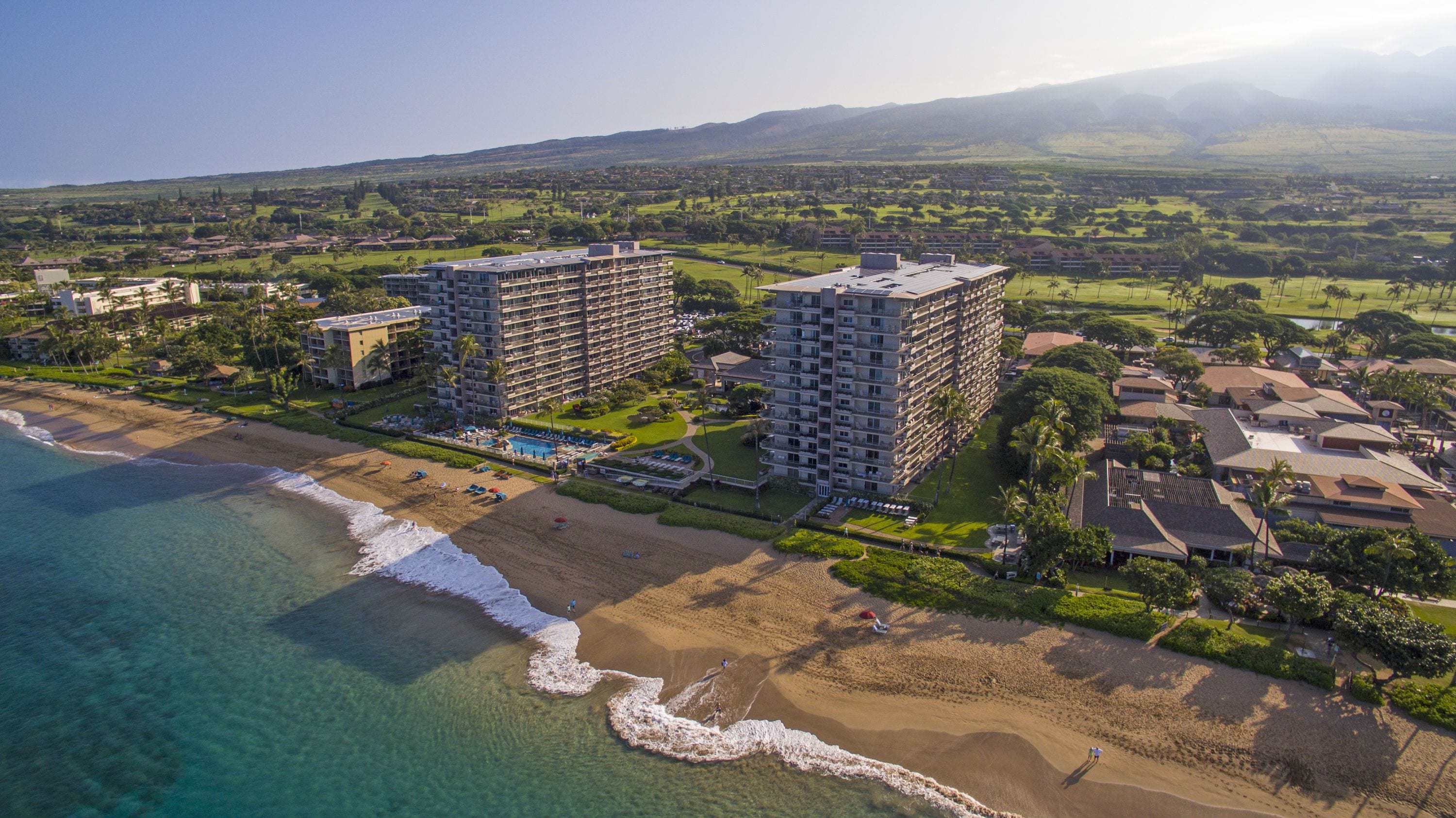 Um hotel à beira-mar com vários edifícios altos, uma praia e um campo de golfe ao fundo.