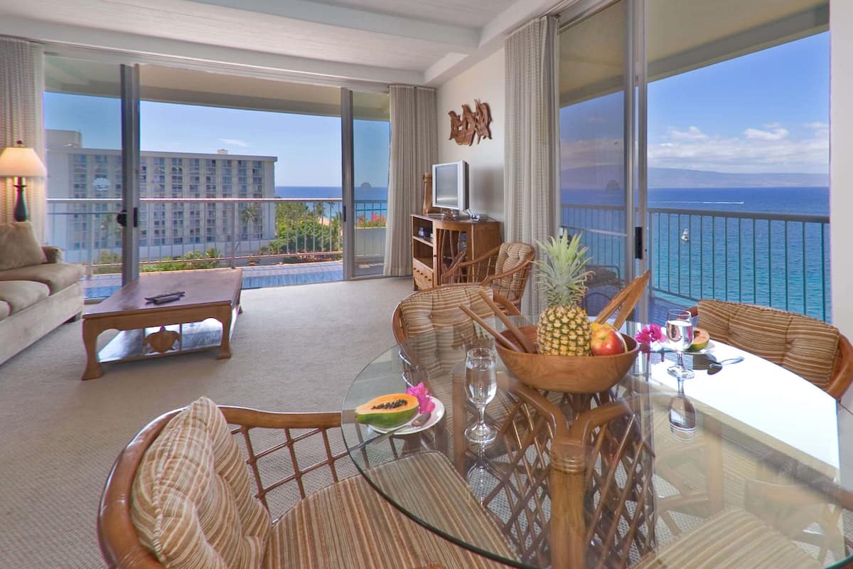 A spacious balcony with a glass table, wicker chairs, and a view of the ocean.
