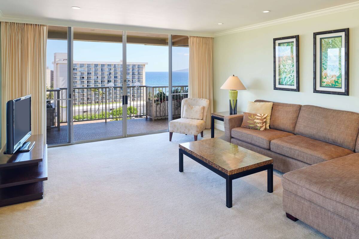 A hotel room with a balcony, a sofa, a chair, a coffee table, and a TV.