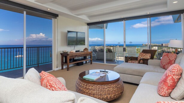 A spacious living room with a large window overlooking the ocean, a comfortable sofa set, a coffee table, and a flat-screen TV mounted on the wall.
