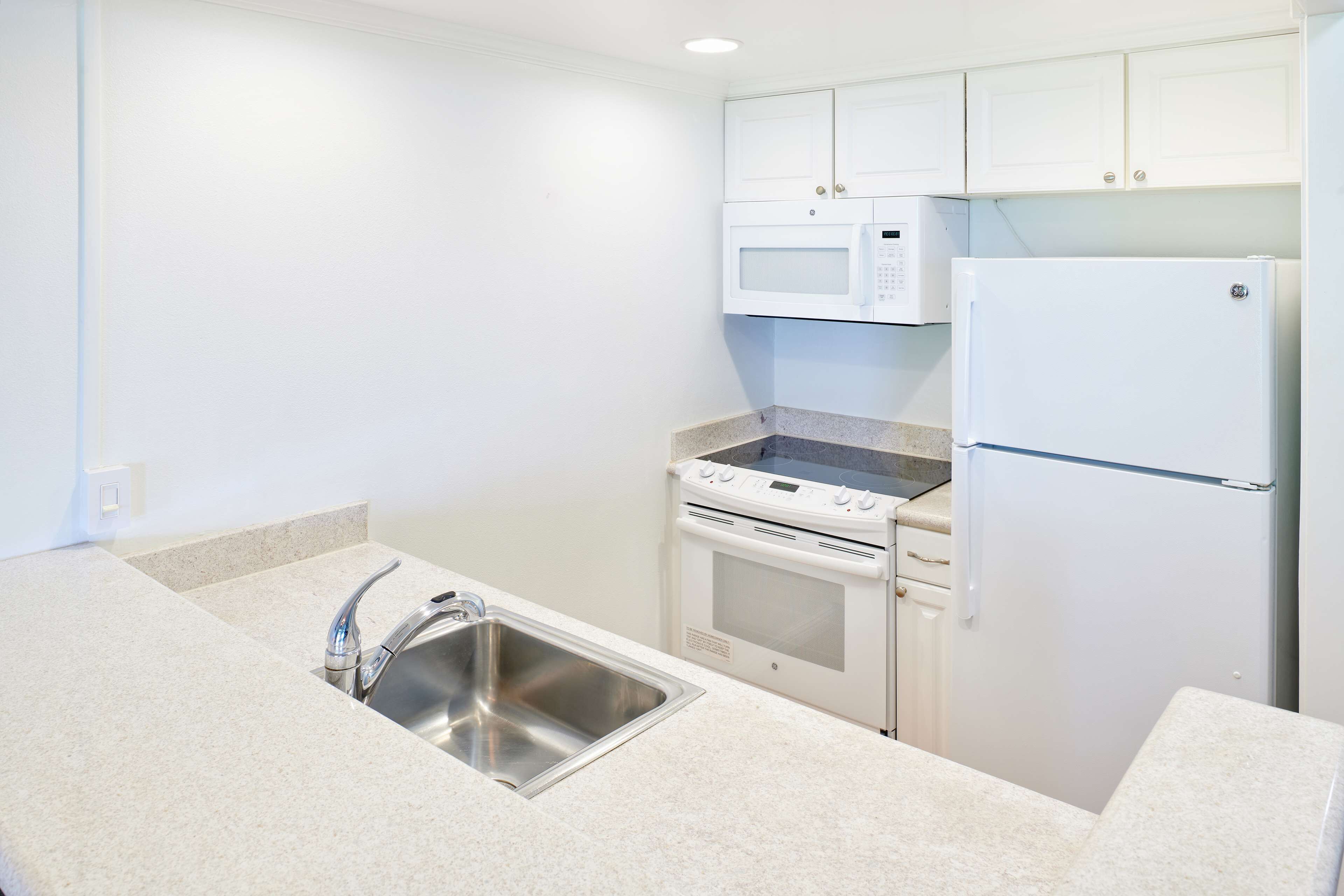 A kitchen with white cabinets, a stainless steel sink, a microwave, an oven, and a refrigerator.