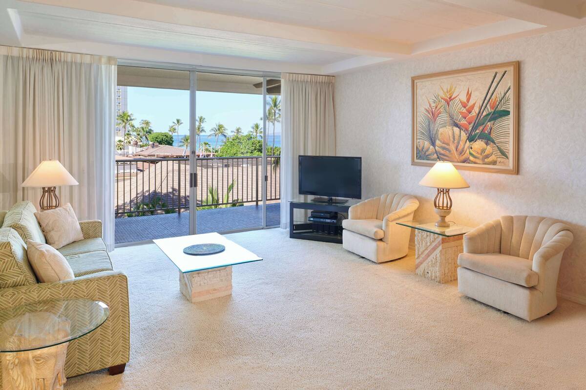 A living room with a sofa, armchairs, a glass coffee table, a TV, and a painting on the wall.