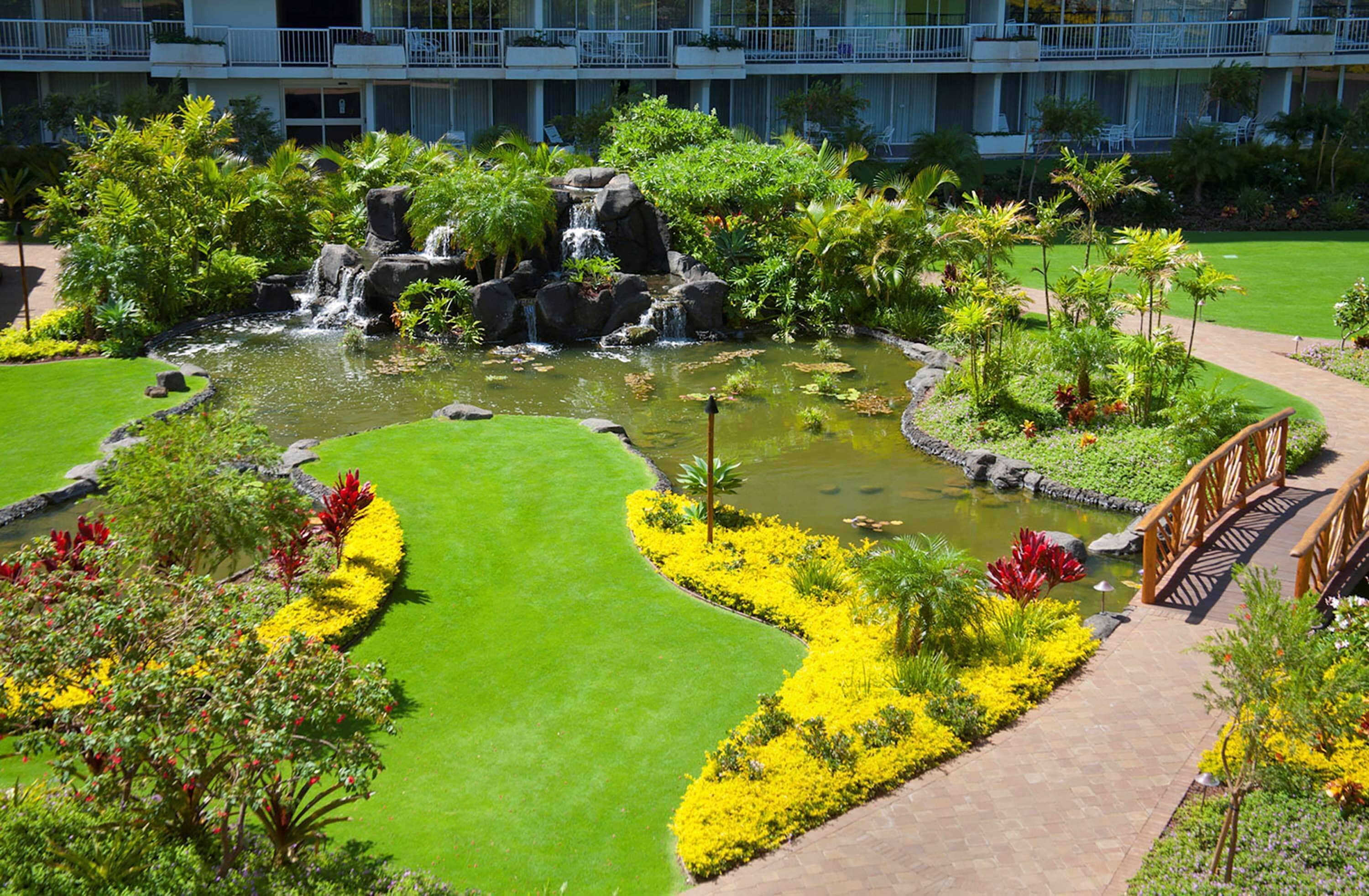 A landscaped garden with a pond, a wooden bridge, and a building in the background.