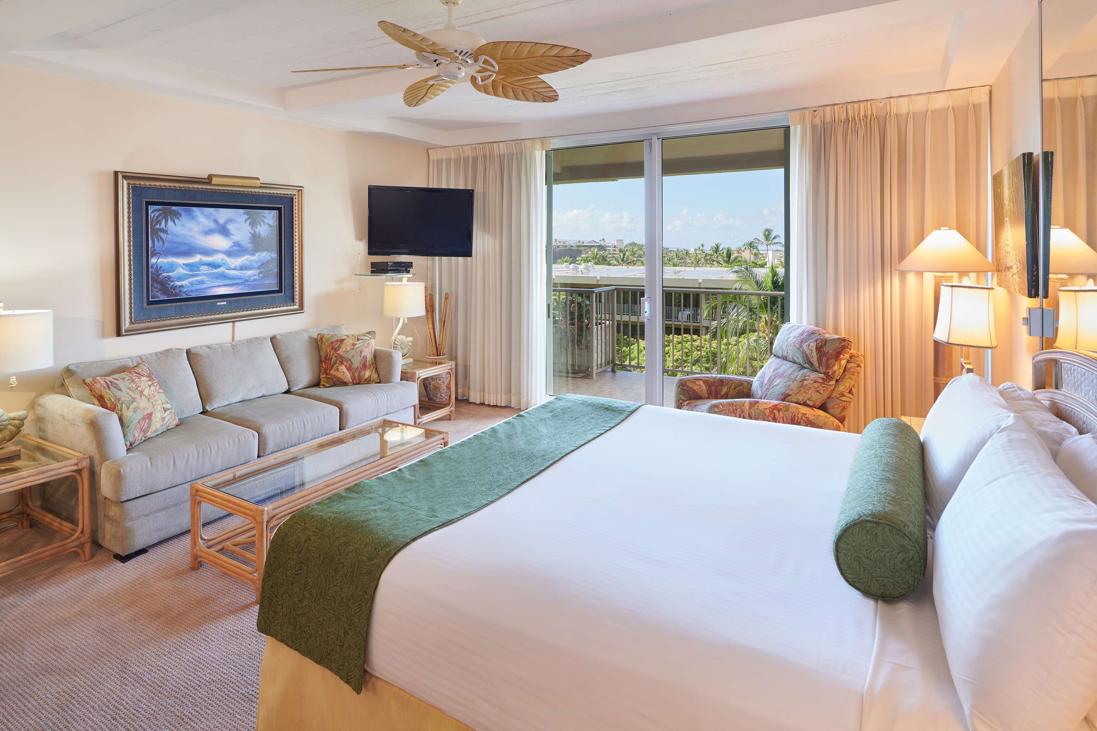 A hotel room with a large bed, a sofa, a coffee table, a TV, and a balcony with a view.