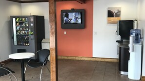 A lobby with a vending machine, a television mounted on the wall, a water dispenser, and a small table with chairs. - Northway Inn Queensbury - Lake George (Queensbury)