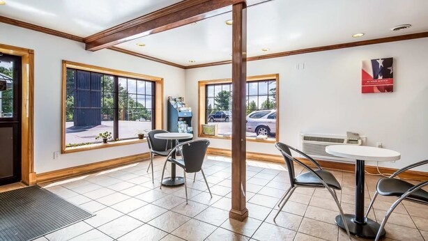 A spacious indoor area with large windows, a central pillar, and a small table with chairs. - Northway Inn Queensbury - Lake George (Queensbury)