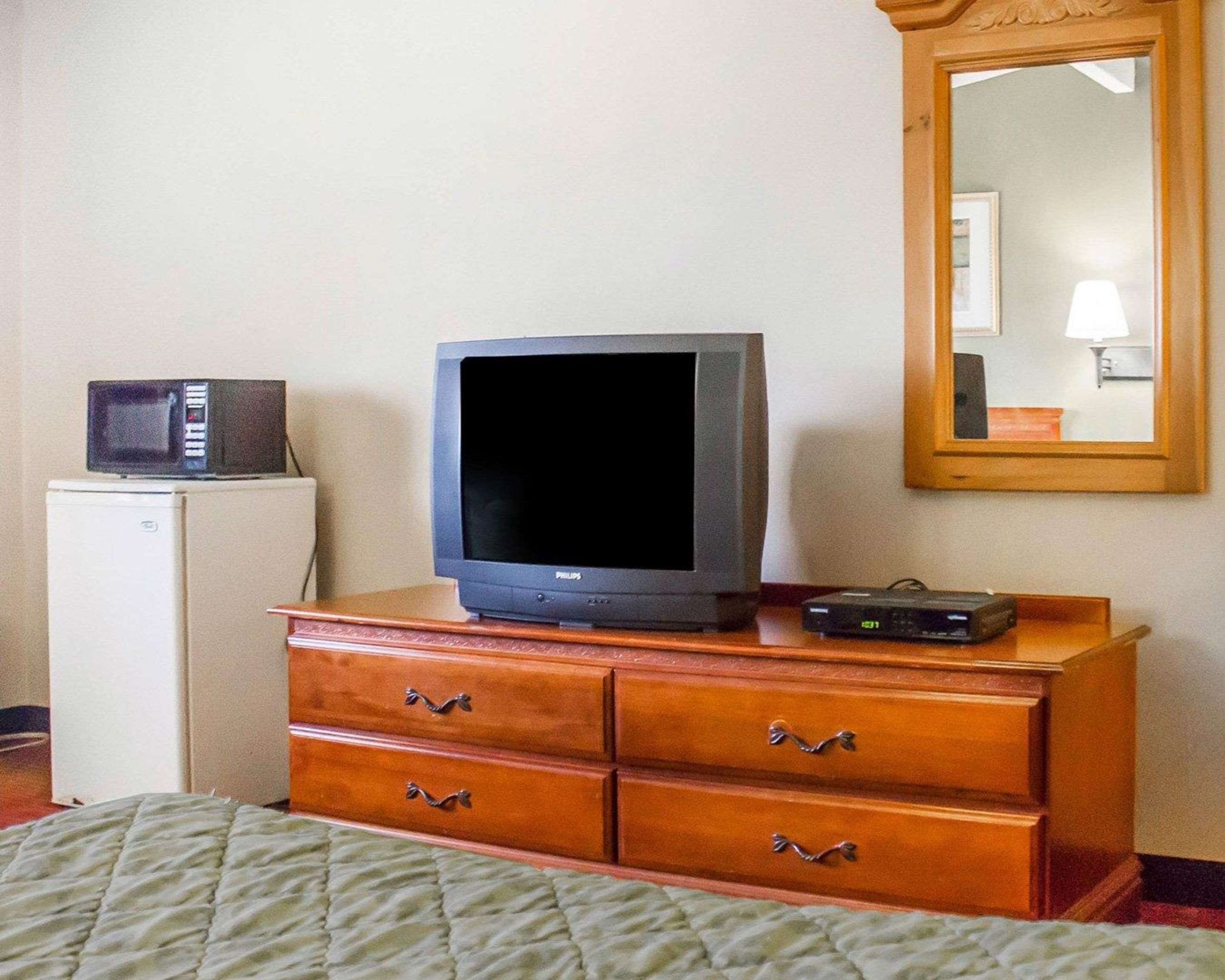 A room with a television on a wooden dresser, a microwave on a small white appliance, and a mirror on the wall.