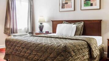 Una habitación de hotel con una cama grande, una mesita de noche con lámpara y dos cuadros en la pared.