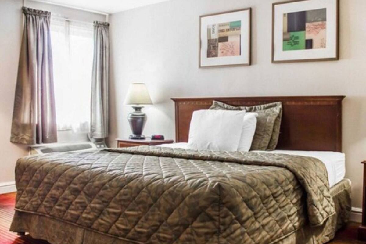 A hotel room with a large bed, a nightstand with a lamp, two framed pictures on the wall, and a window with curtains.