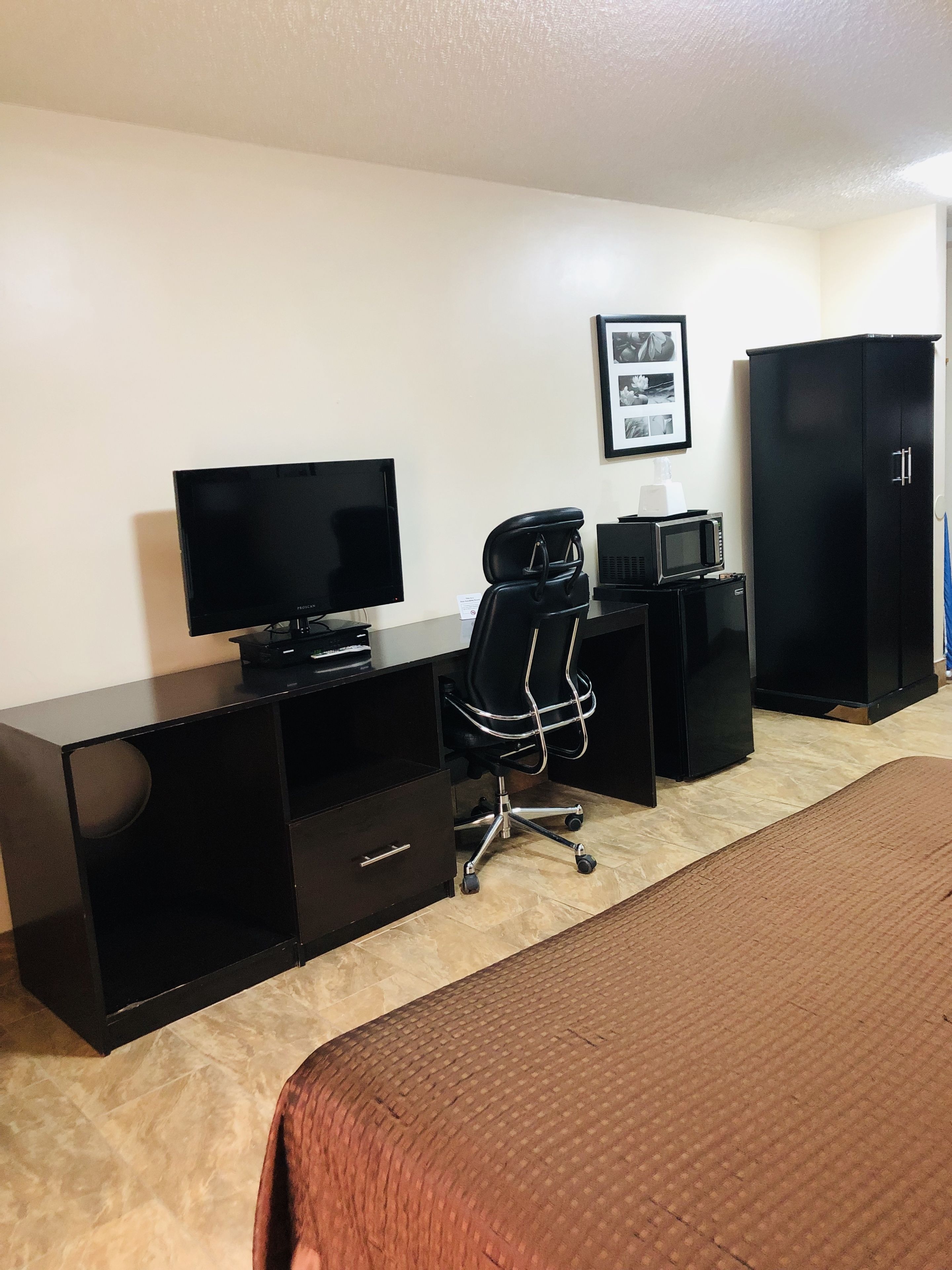 A hotel room with a bed, a desk with a computer, a chair, a television, a microwave, and a wardrobe.