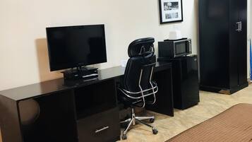 A hotel room with a bed, a desk with a computer, a chair, a television, a microwave, and a wardrobe.