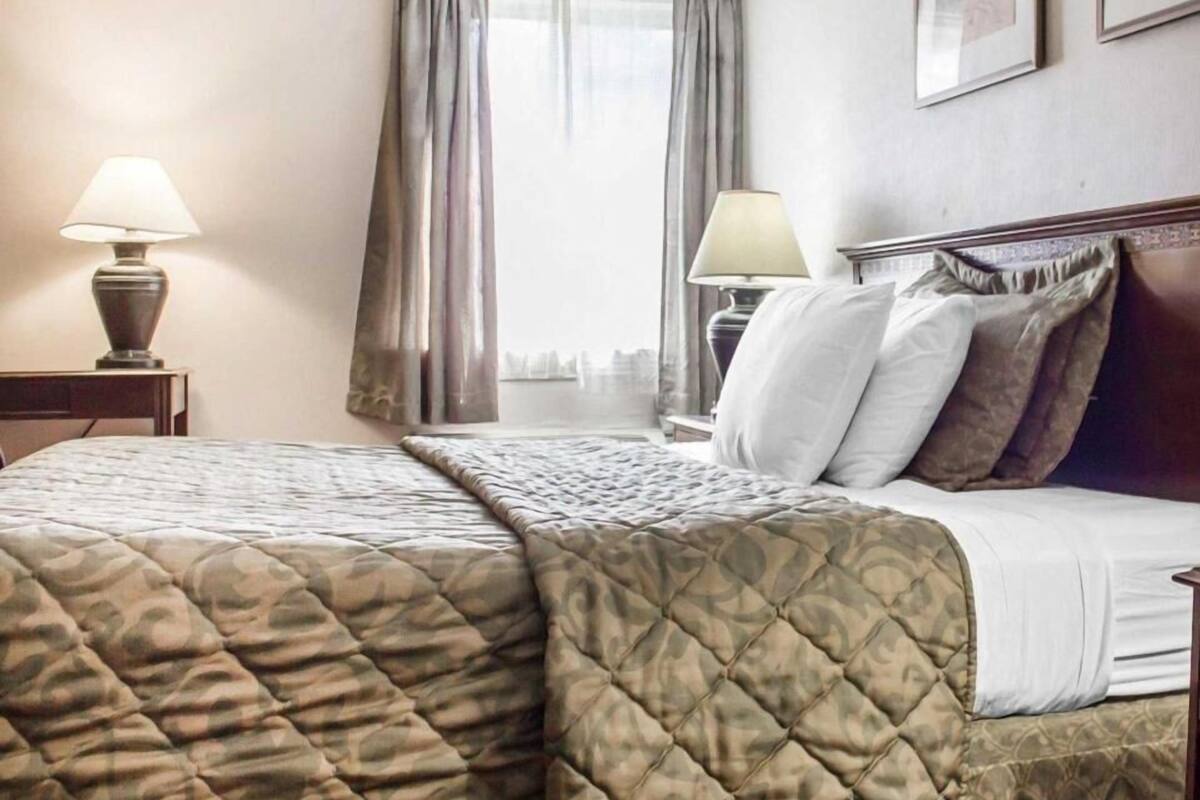 A hotel room with a bed, two bedside lamps, a nightstand, and a window with curtains.