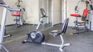 Un gimnasio con máquinas de cardio, equipo de levantamiento de pesas y un espejo grande.