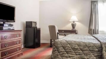 A hotel room with a bed, a desk with a lamp, a television on a dresser, and a chair.
