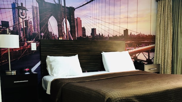 Habitación de hotel con una cama, una mesita de noche, una lámpara y un mural grande con una vista urbana.