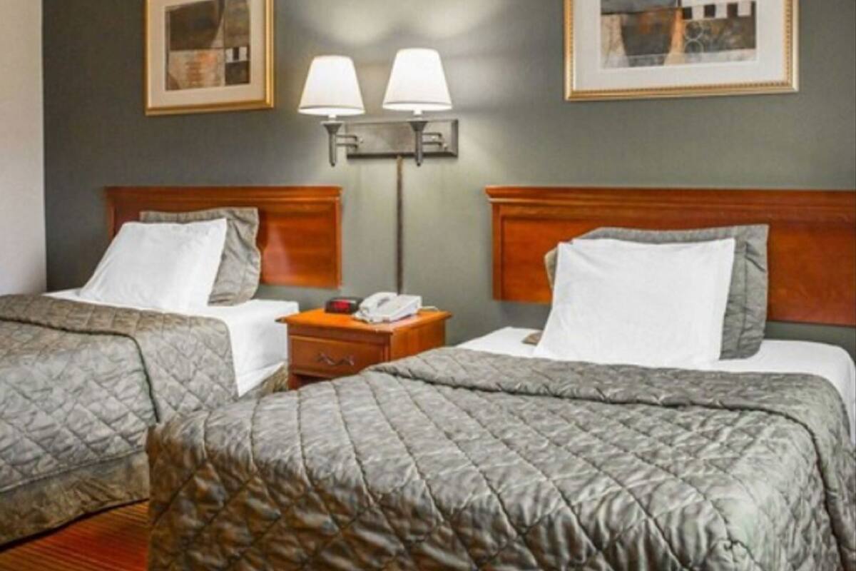 A hotel room with two beds, a nightstand with a lamp, and two framed pictures on the wall.