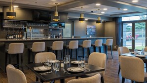 Un bar moderno con barra, taburetes y una zona de comedor con mesas preparadas para dos.