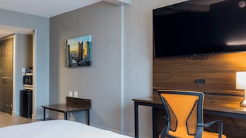 A hotel room with a bed, a desk with a chair, a television, and a painting of a cityscape.