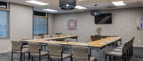 A conference room with long tables, chairs, and a large screen.