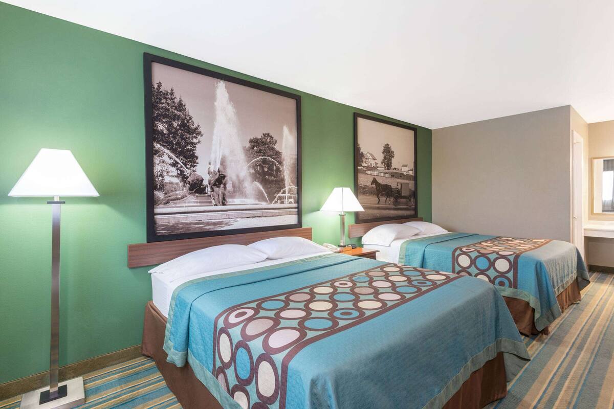 A hotel room with two beds, green walls, and two framed pictures.