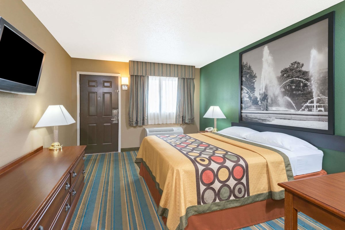 A hotel room with a bed, two bedside lamps, a flat-screen TV, a door, and a window with curtains.