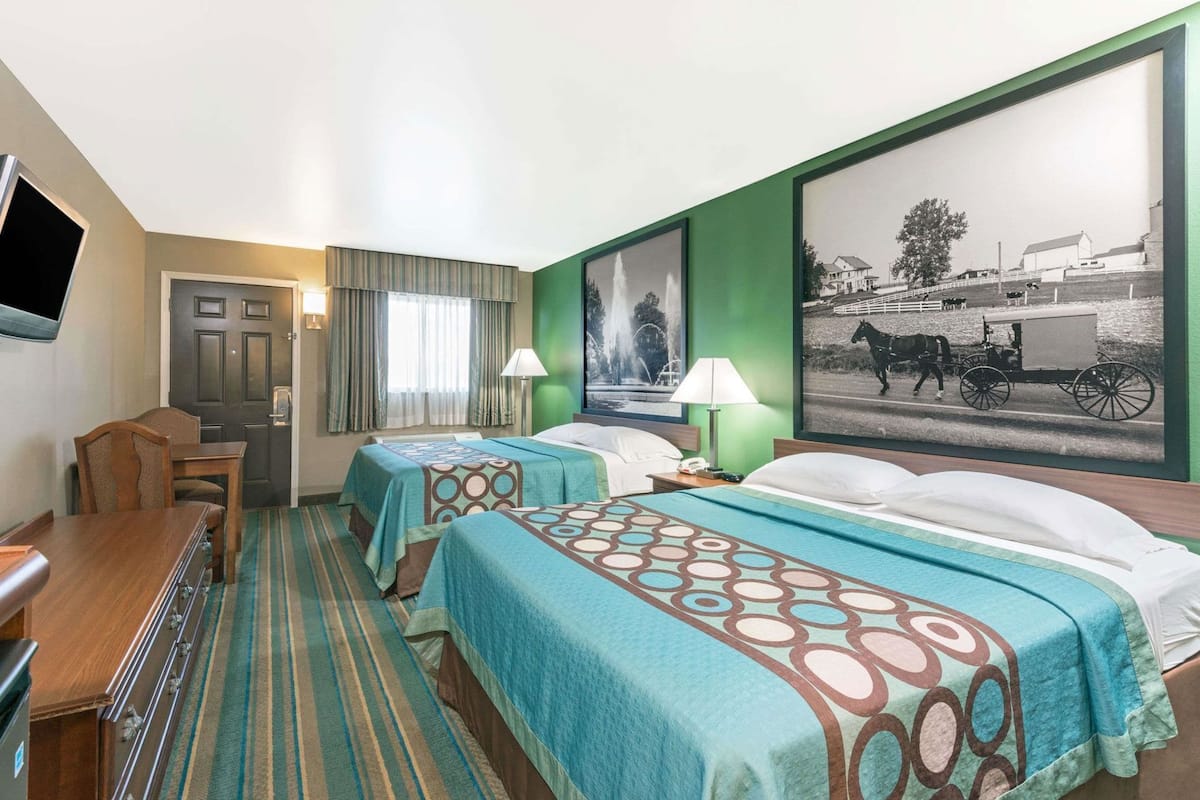 A hotel room with two beds, a desk, a chair, a television, and a large framed picture on the wall.
