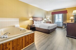 A hotel room with a large bathtub, a double bed, a desk, and a chair.