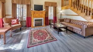 A living room with a fireplace, a sofa, a chair, a coffee table, and a staircase. - Quality Inn Greenville North (Greenville)