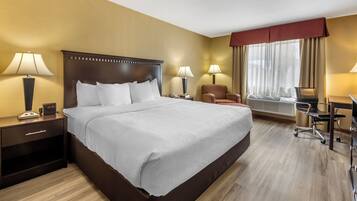 A hotel room with a large bed, two bedside tables with lamps, a chair, a desk, and a window with curtains.