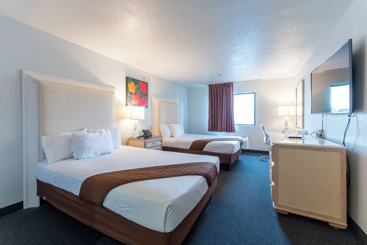 Une chambre d’hôtel avec deux lits, un bureau, une commode, une télévision et une fenêtre avec des rideaux.