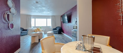 A modern living room with a round table, two armchairs, a sofa, and a TV mounted on the wall.