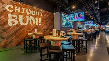 A restaurant with wooden walls and tables, a large screen displaying a show, and a sign that reads "CHIQUITI BUM!".
