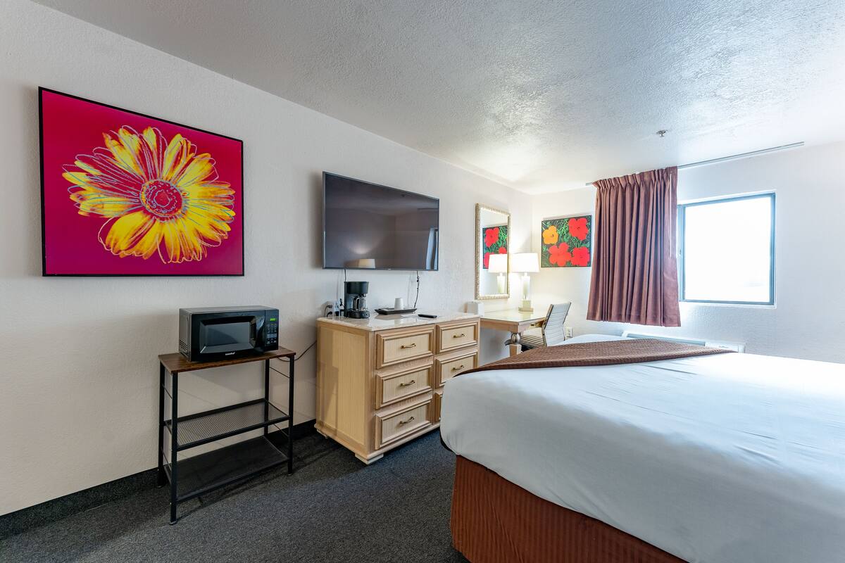 Une chambre d’hôtel équipée d’un lit, d’un bureau avec un ordinateur, d’une télévision et décorée avec des œuvres d’art.