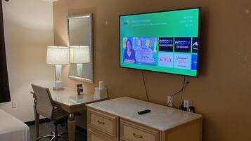 A hotel room with a bed, a desk, a mirror, a TV mounted on the wall displaying a welcome message, and a dresser.
