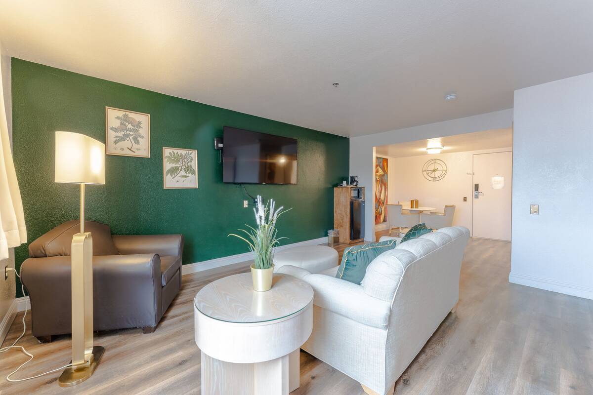 Un salon moderne avec un mur d’accent vert, un téléviseur à écran plat, un canapé, une table basse et une lampe.