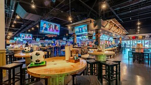 A bar area with multiple screens displaying content, wooden tables, and stools. - Hotel Jefe at Ojos Locos- No Resort Fee (North Las Vegas)
