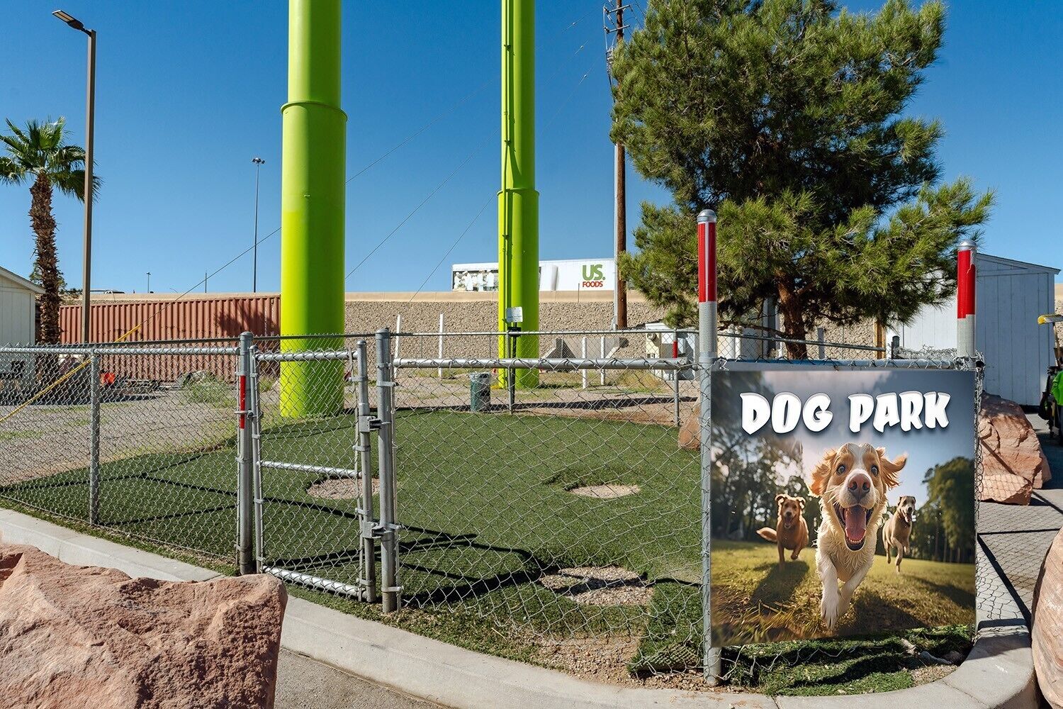A fenced dog park with a sign, green poles, and a clear sky.