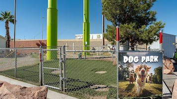 A fenced dog park with a sign, green poles, and a clear sky.