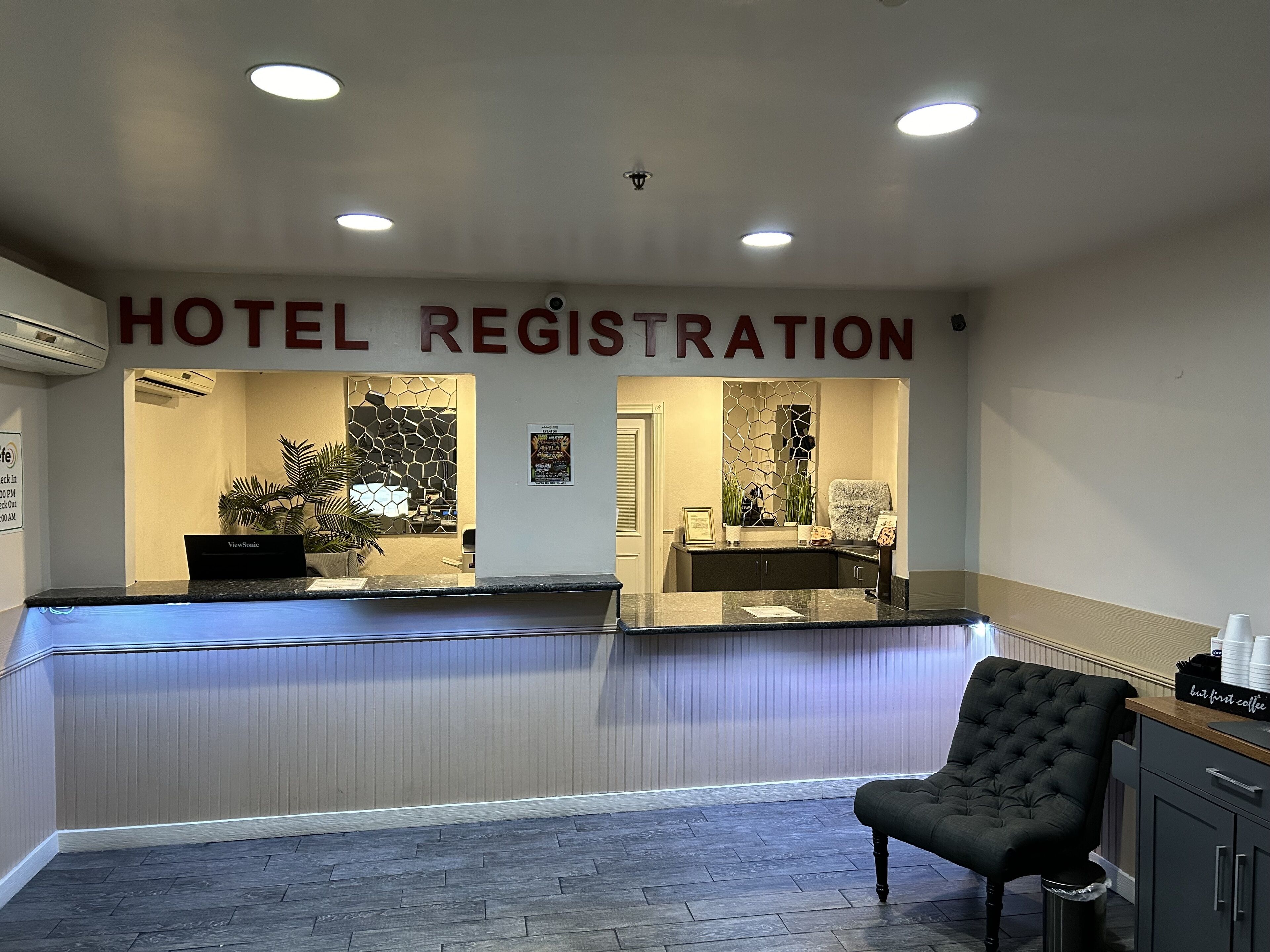A hotel registration desk with a reception area, a chair, and a cabinet with a coffee machine.