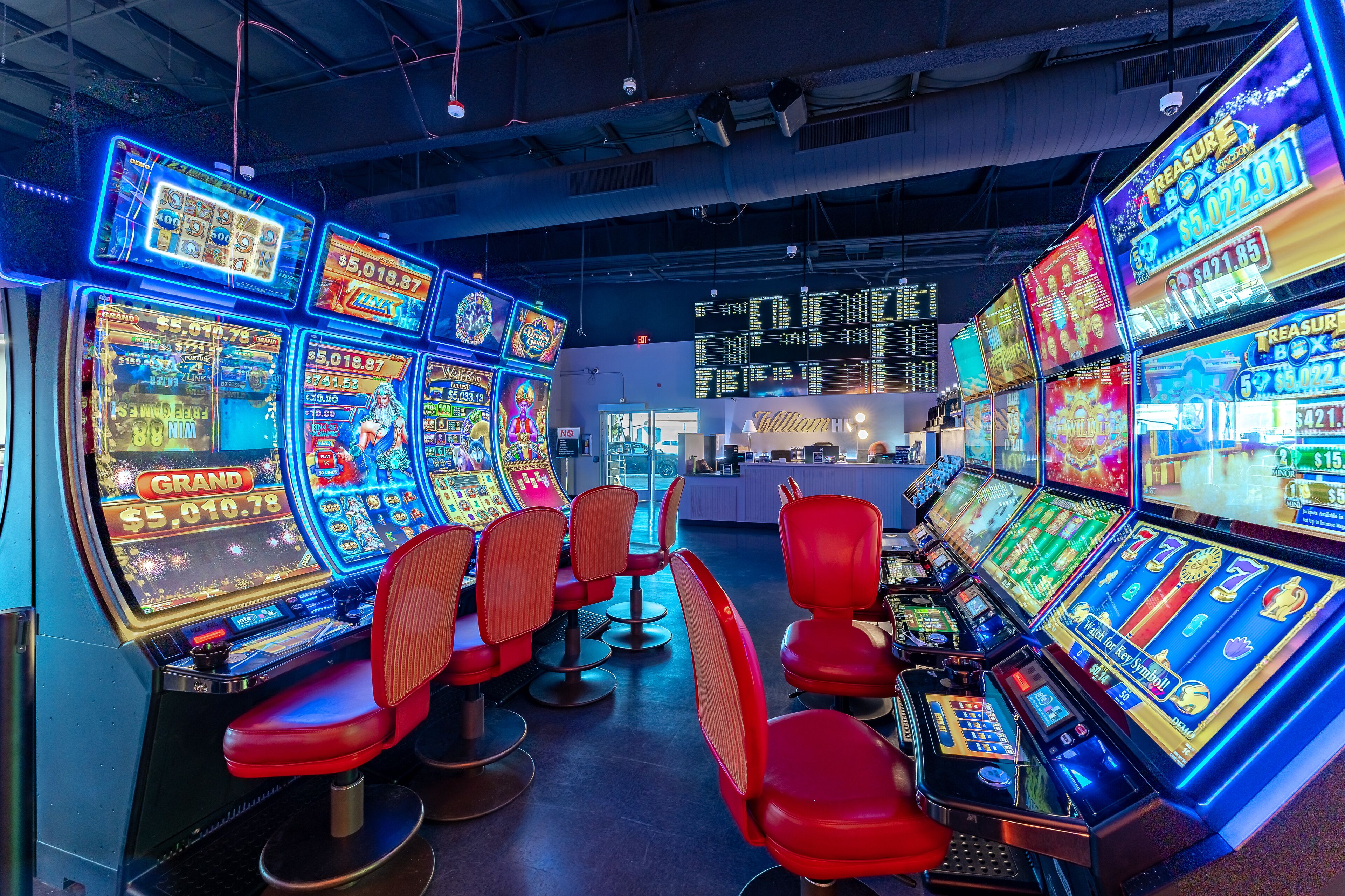 A casino with multiple slot machines and red chairs.