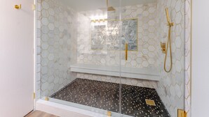 A glass-enclosed shower with a geometric tile pattern and a gold showerhead. - Hotel Jefe at Ojos Locos- No Resort Fee (North Las Vegas)