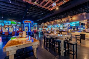 Une salle d’arcade avec plusieurs écrans et des tables en bois.